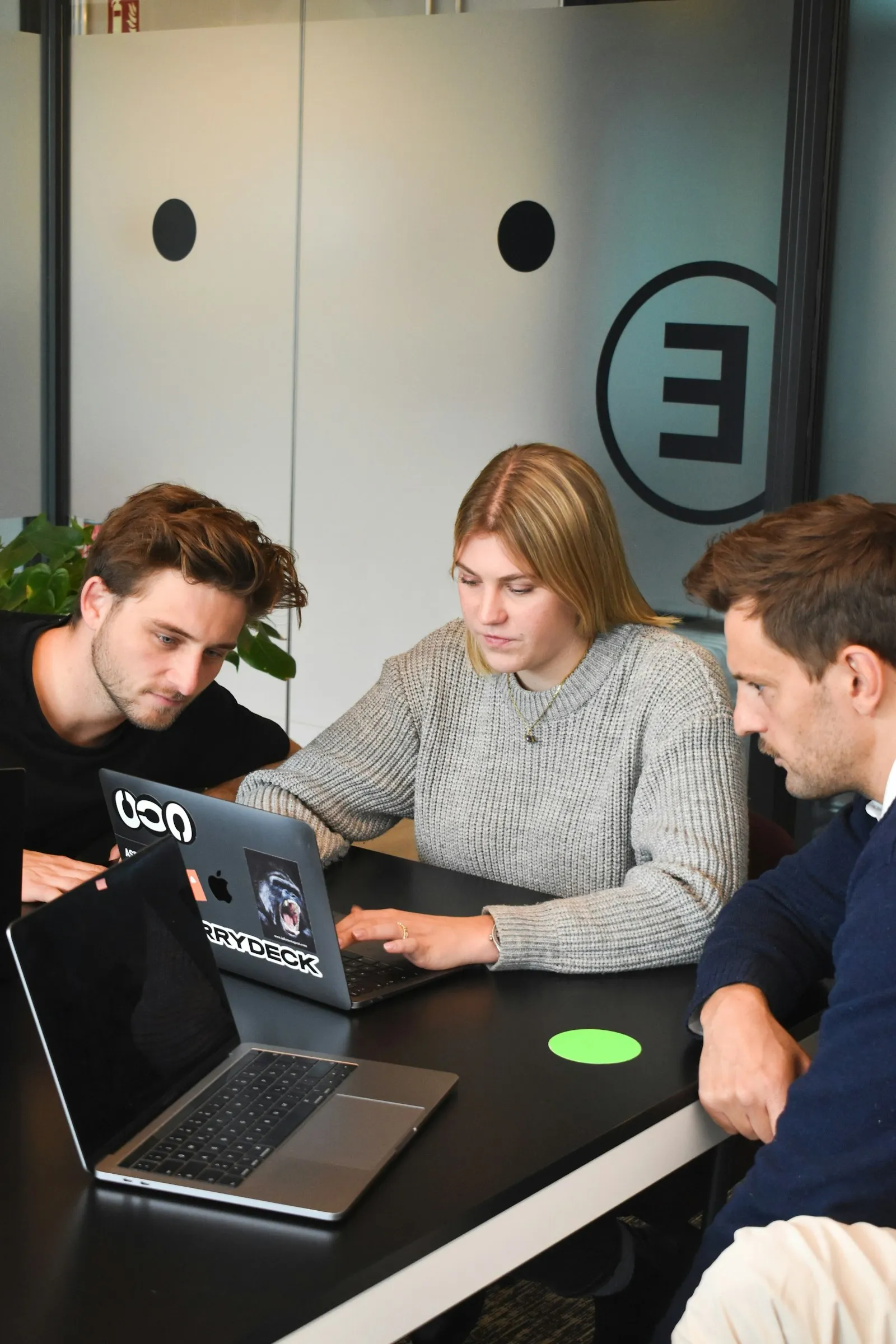 Three people collaborating on a laptop at a table in an office