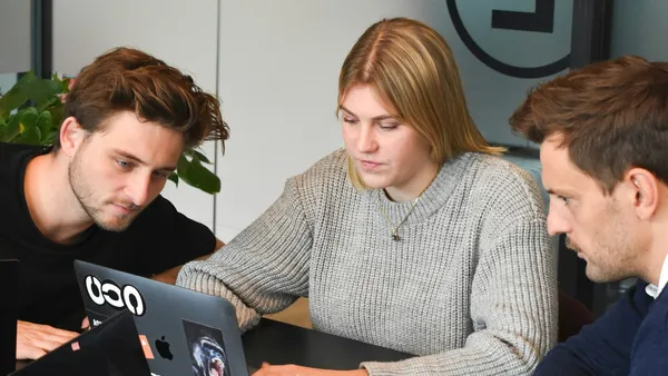 Three people collaborating on a laptop at a table in an office