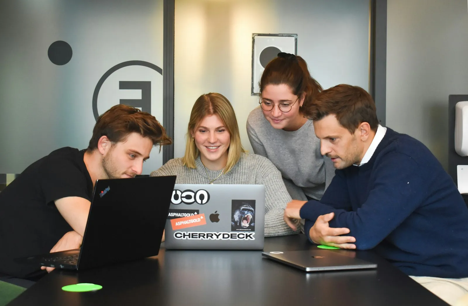 Four people collaborating around a laptop in a modern office