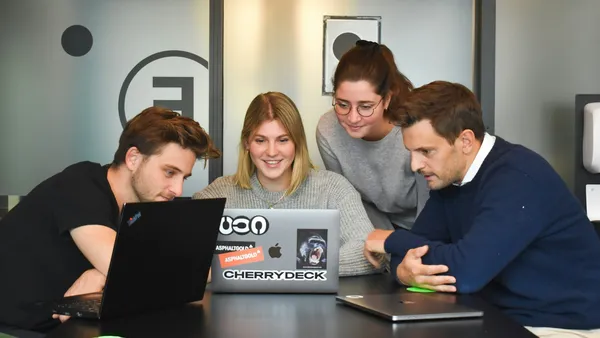 Four people collaborating around a laptop in a modern office
