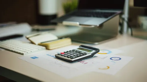 Calculadora sobre informes impresos de costos y presupuesto junto a una laptop