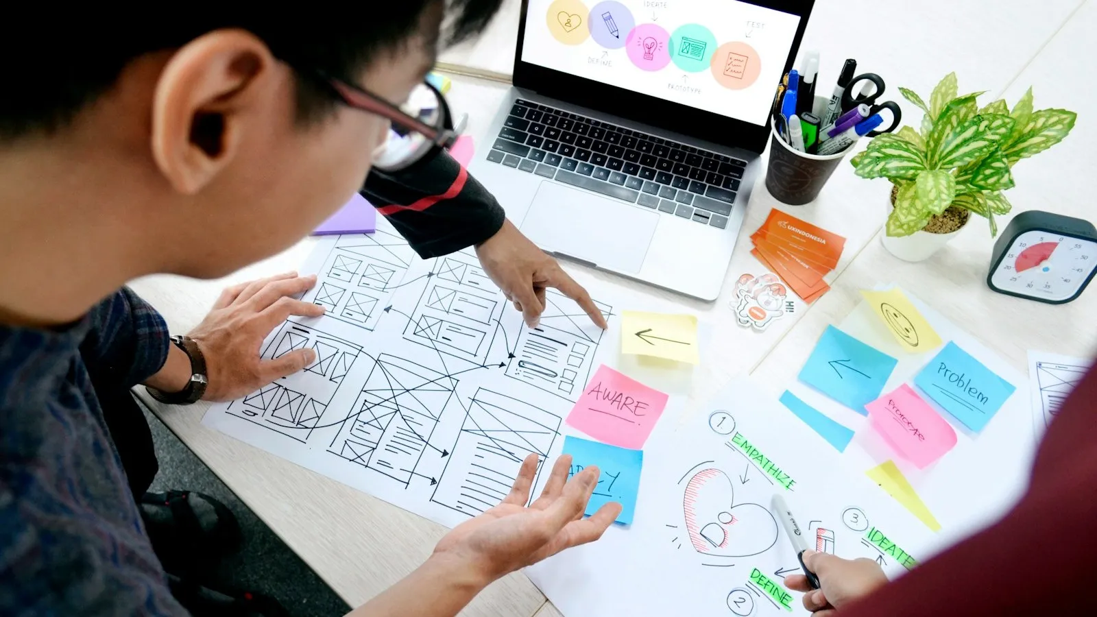 Designer mapping product wireframes at a desk beside a laptop