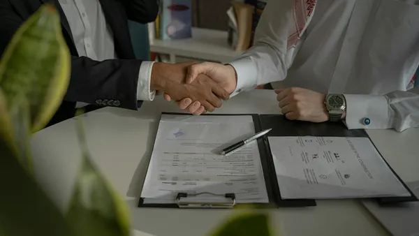Dos personas dÃ¡ndose la mano sobre un contrato firmado en un escritorio