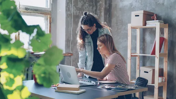 Two colleagues reviewing design work together on a laptop