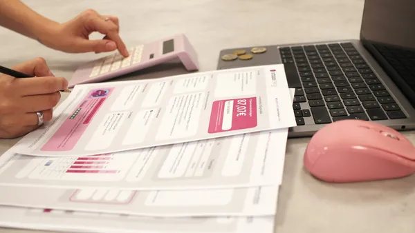 Someone calculating costs with a calculator and printed reports