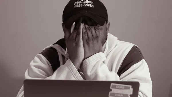 Person sitting at a laptop with hands over their face